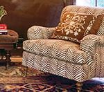 Armchair with brown and white chevron pattern, brown floral pillow, next to small table with books.