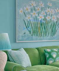 Green couch with turquoise throw pillows next to a blue wall with a daffodil painting.