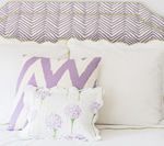 Bed with a lavender chevron headboard and pillows in matching shades, with a white bedspread.