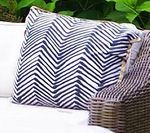 Blue and white zig-zag patterned decorative pillow on a white outdoor sofa, near wicker furniture.