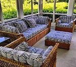 Wicker patio furniture with blue patterned cushions on a sun porch, overlooking a green yard.