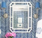 White framed mirror with blue sconces on patterned wallpaper.