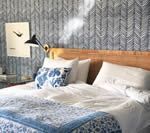 Bedroom with blue patterned wallpaper, wooden headboard, and bed covered in white linens and blue patterned quilt.