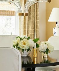 Table setting with flower arrangements, gold accents, and a lamp near a window.