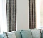 Teal sofa with decorative pillows, brown plaid curtains, and a white wall.