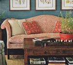 Pink sofa with pillows in front of a blue wall; a dark wood coffee table and framed art are in the foreground.