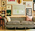 Sofa with several framed art pieces on a pale pink wall. The sofa is grey and has two patterned pillows.
