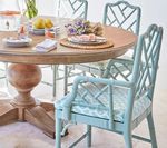 Round wooden dining table set with light blue bamboo-style chairs, set with plates and flowers.