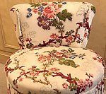 Upholstered chair with a floral pattern, featuring pink, red, and blue flowers on a white background.