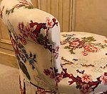 Chair with floral upholstery in pink, red, and green against a beige background.
