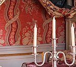Candelabra with three lit candles in front of red floral wallpaper and a draped valance.