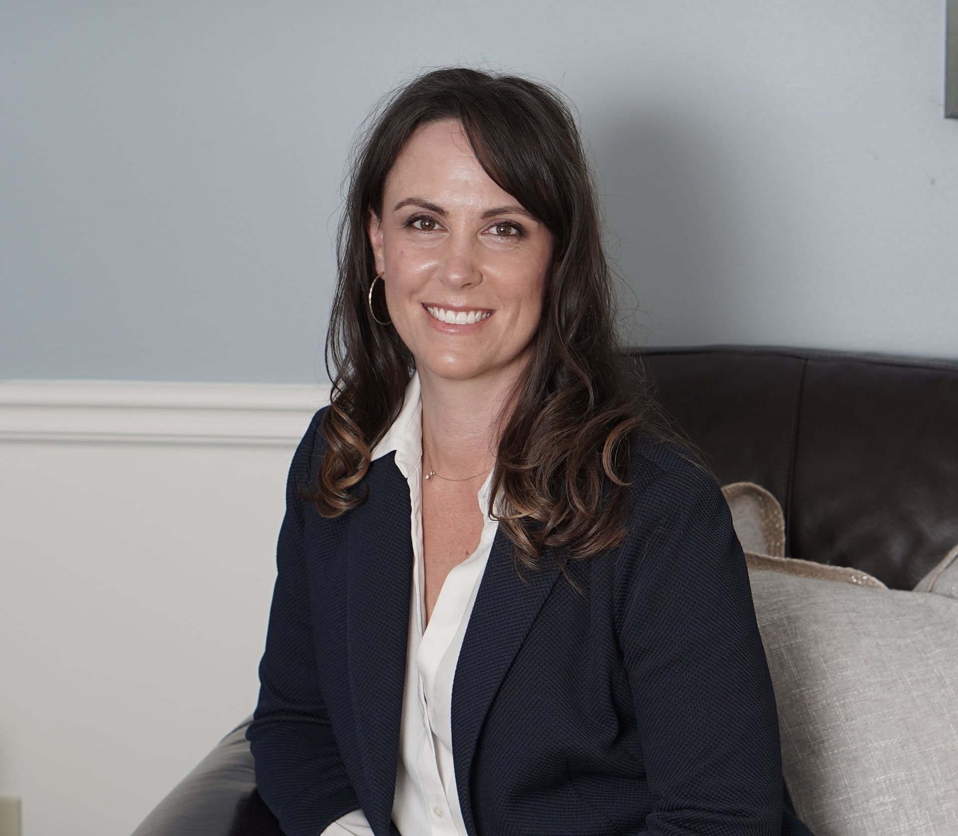 A woman in a suit is sitting in a chair and smiling.