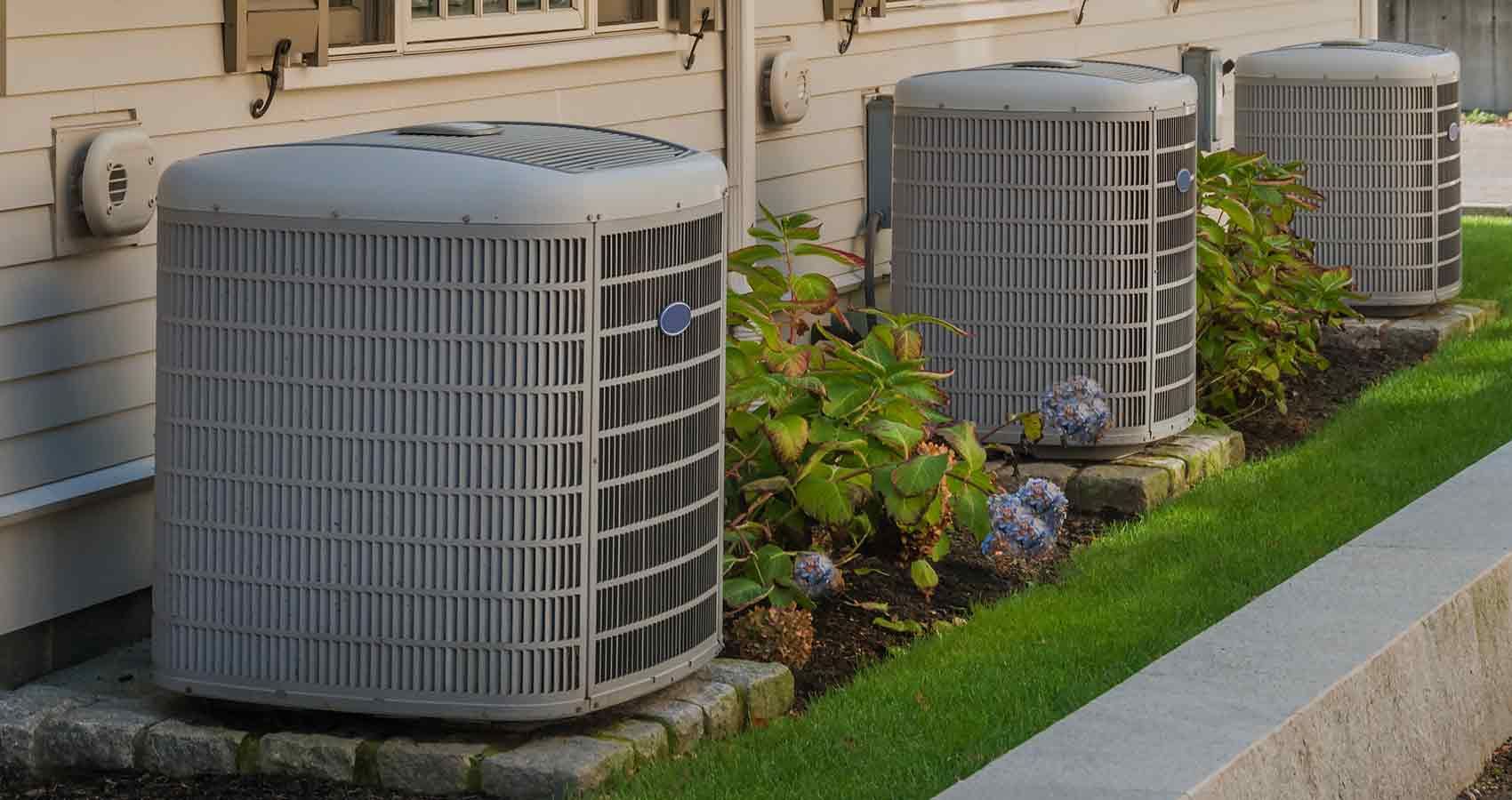 A row of air conditioners are sitting on the side of a house.