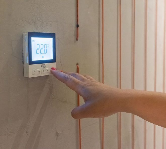 Uma pessoa está pressionando um botão em um termostato, demonstrando como é o sistema de piso aquecido enerpro