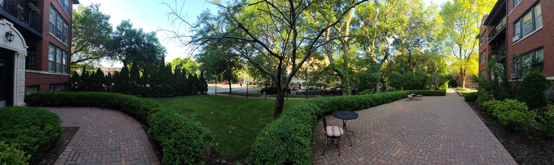 A panoramic view of a park surrounded by trees and bushes in front of a brick building.