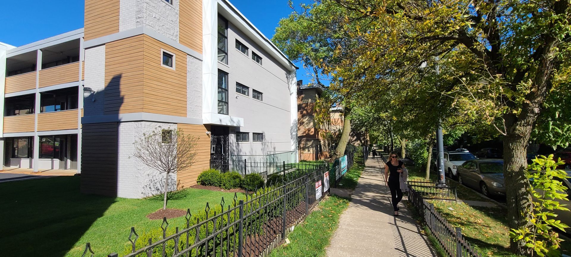 A man is walking down a sidewalk in front of a large building.