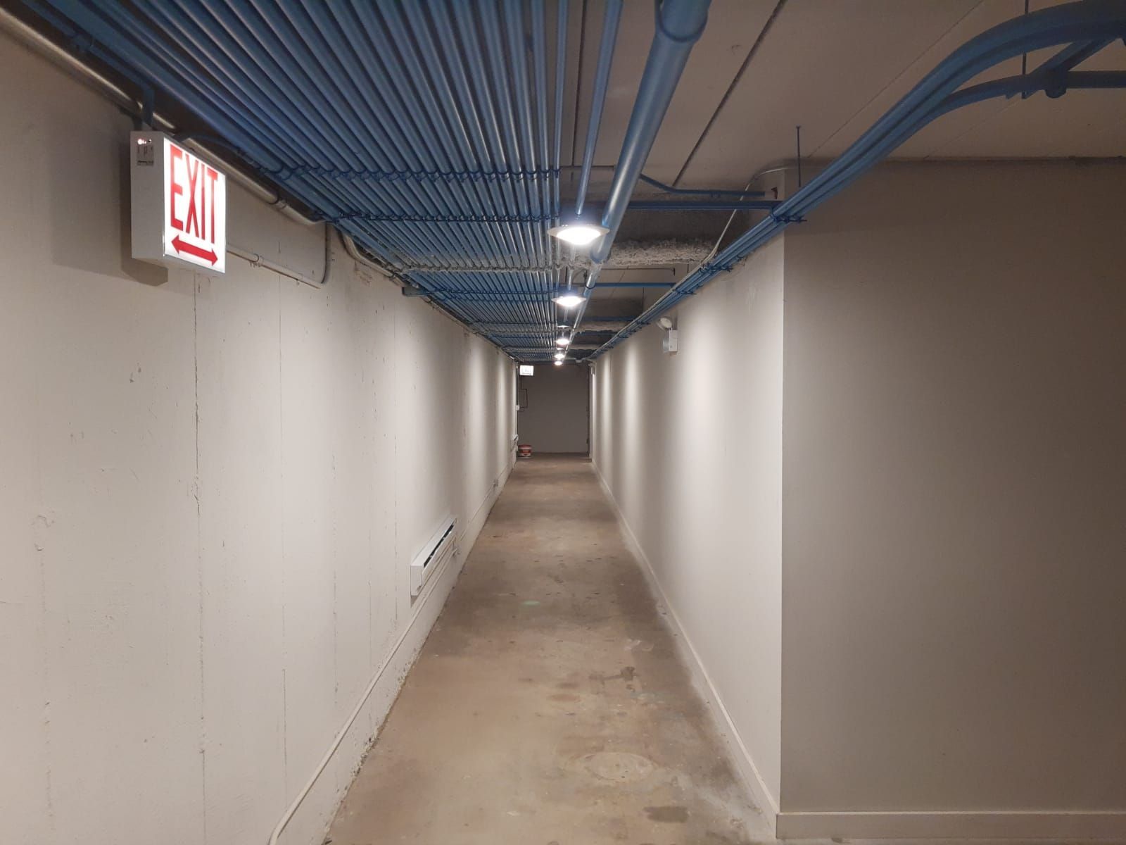A long hallway with a red exit sign on the wall.