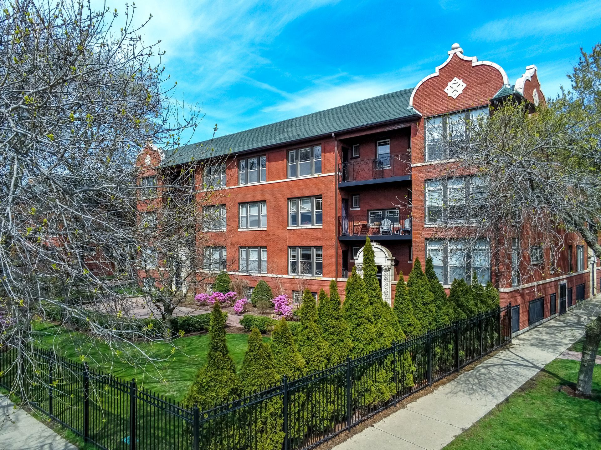 A large brick apartment building with a fence around it and trees in front of it.