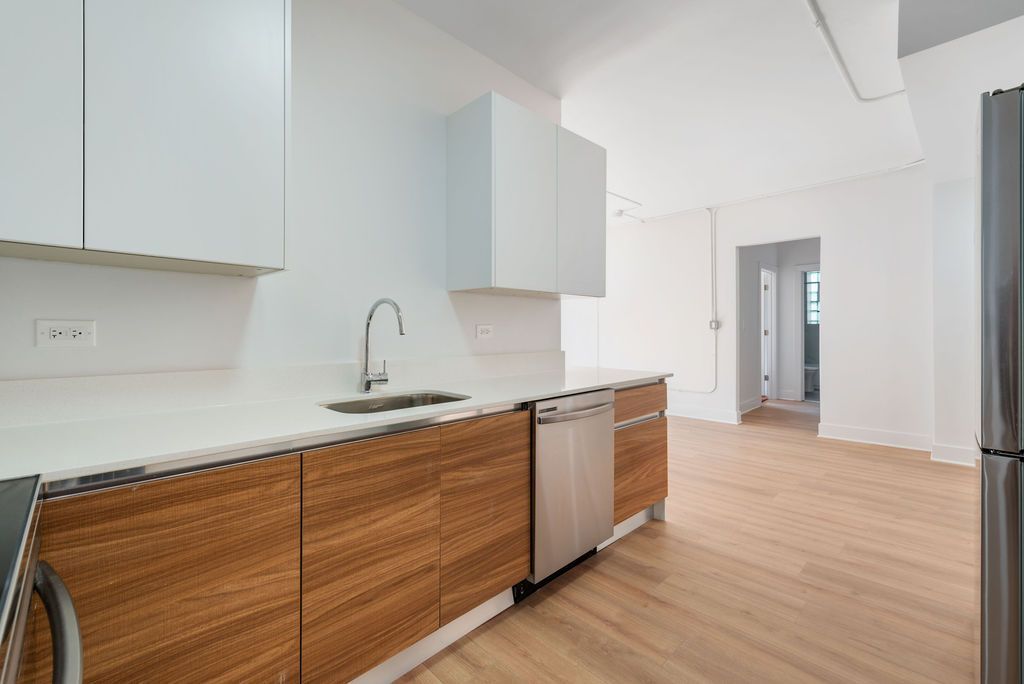 A kitchen with wooden cabinets , stainless steel appliances , a sink and a refrigerator.