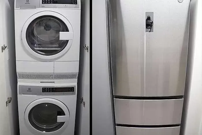 A washer and dryer are stacked on top of each other next to a refrigerator.