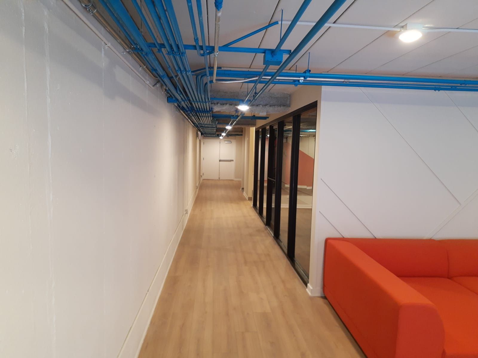 A long hallway with a red couch and blue pipes on the ceiling.