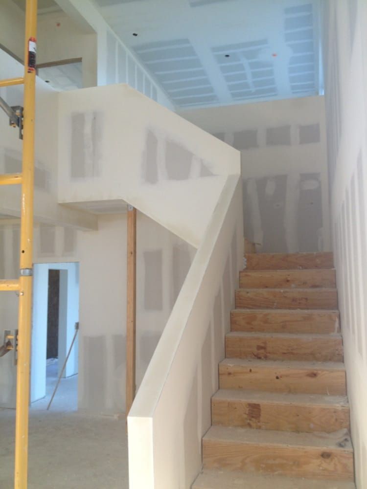 Staircase under construction with wood steps, white walls, and exposed framing in a bright interior.