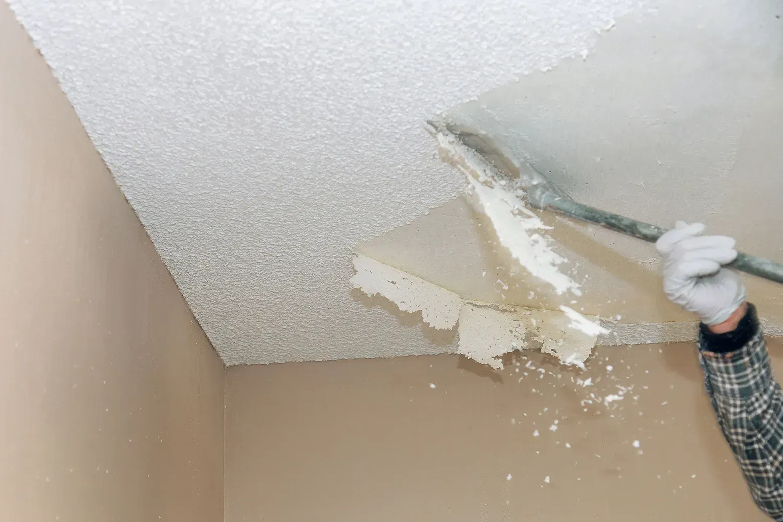 Person scraping damaged popcorn ceiling with a putty knife; peeling plaster falling down.