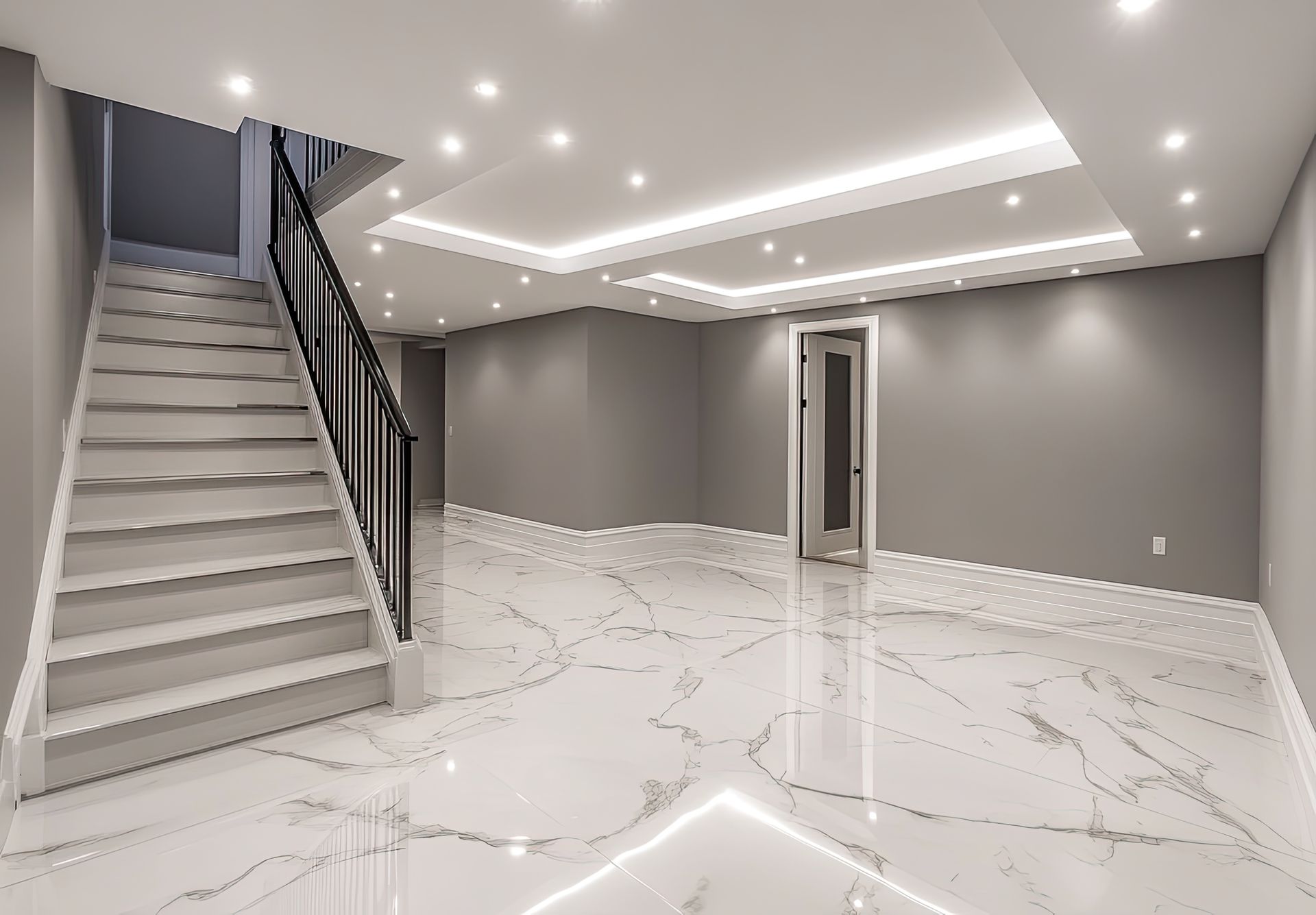 Empty basement room with white marble-look floor and gray walls. Stairs on the left, recessed lighting.