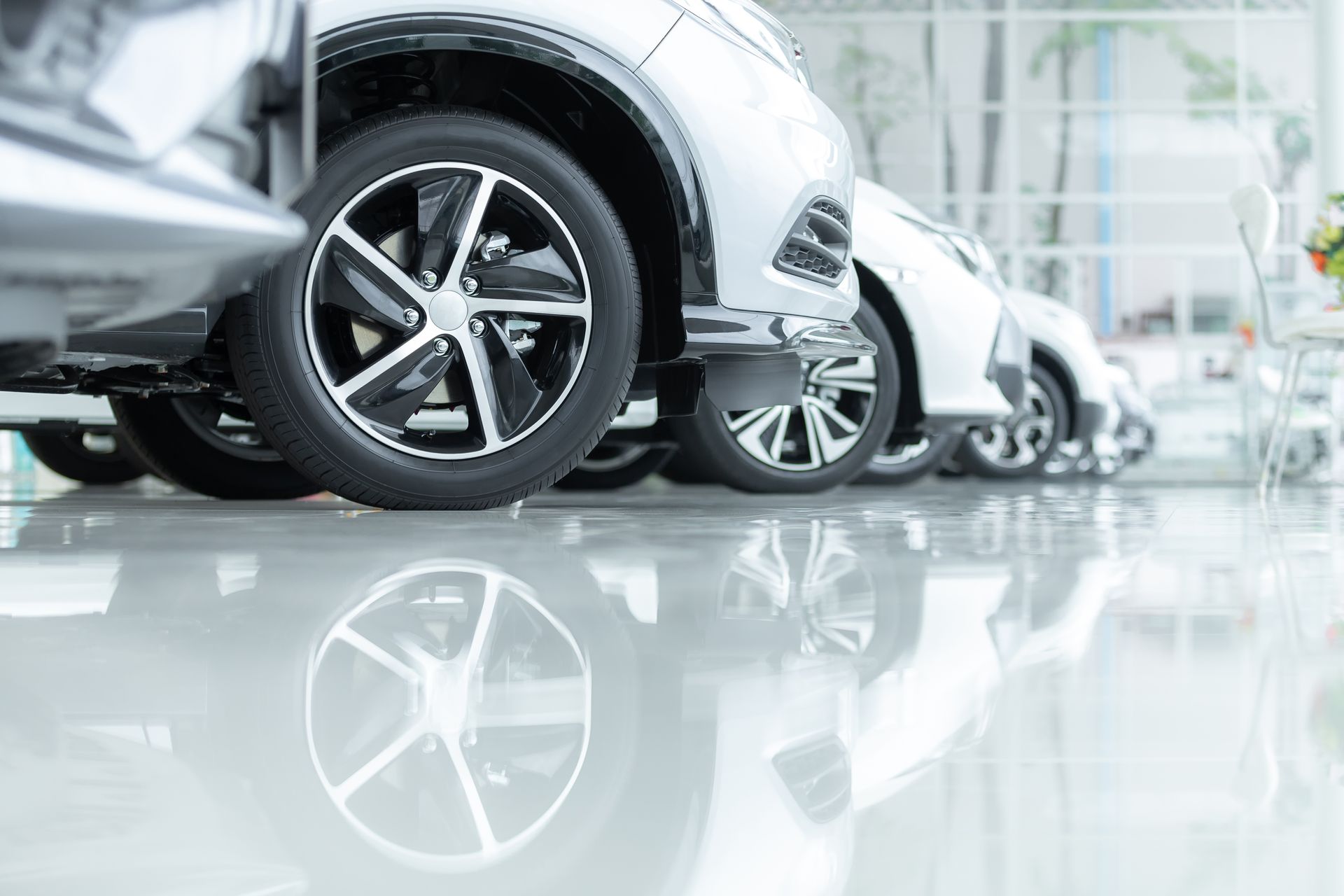 Silver cars parked in a showroom, wheels in focus with reflections on the glossy floor.