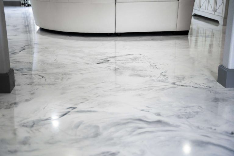 High-gloss, marbled epoxy floor in shades of white and gray, reflecting a white sofa and room details.