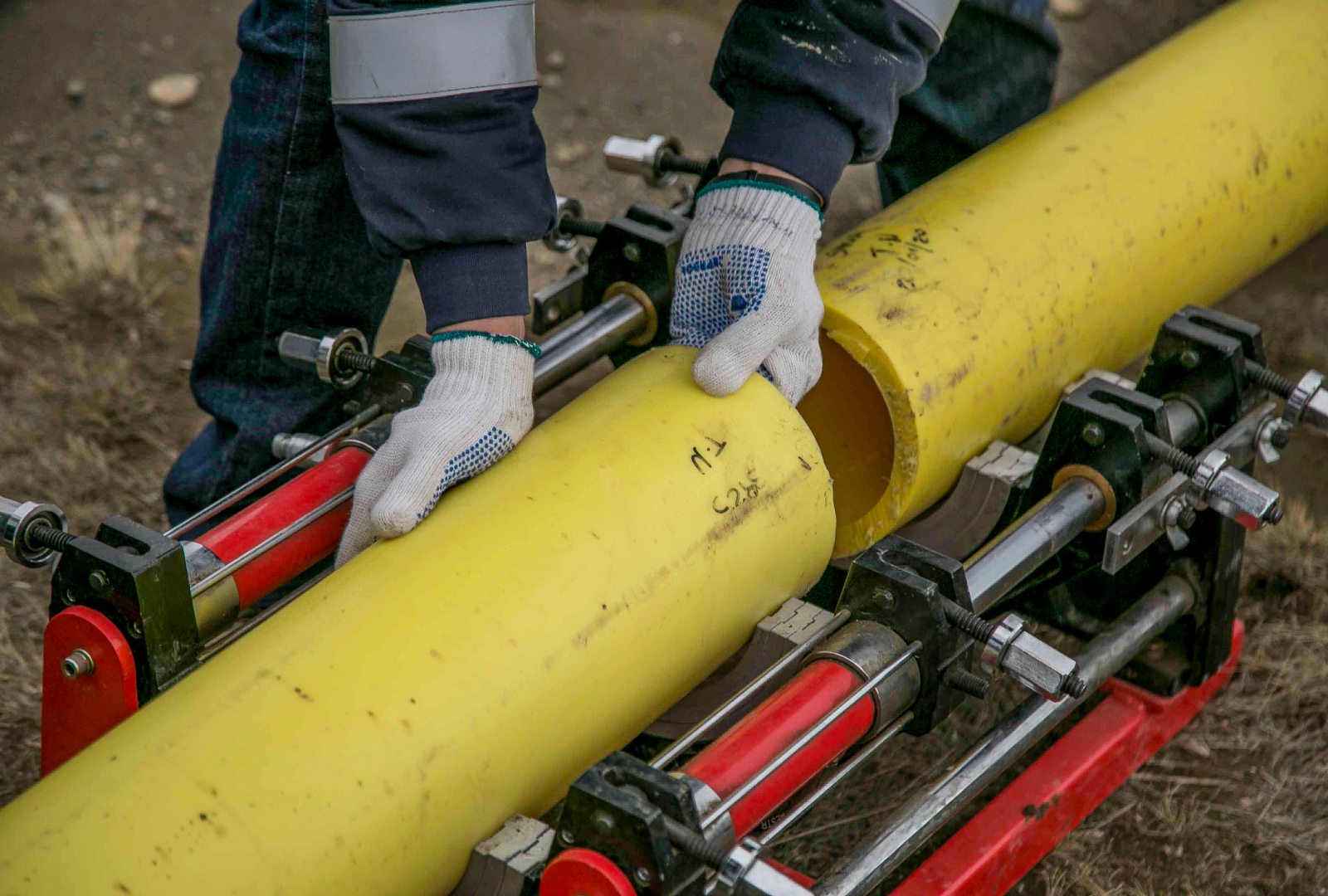 A person in work clothes uses a specialized machine to align two yellow HDPE pipes for welding outdoors.