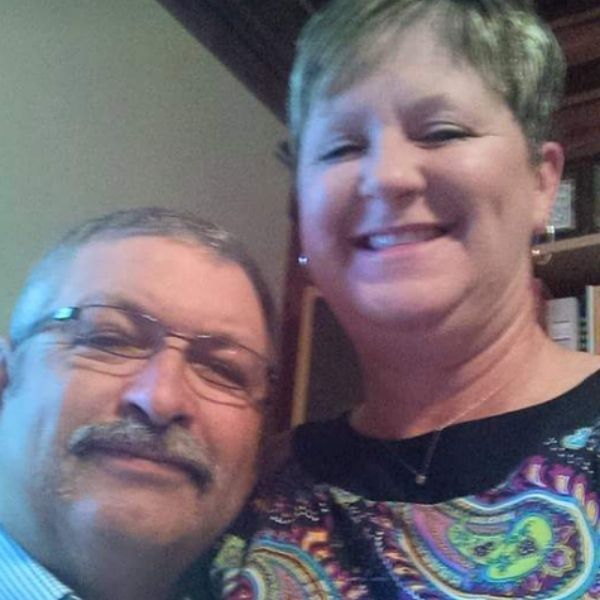 A smiling couple poses for a close-up selfie in front of a bookshelf.