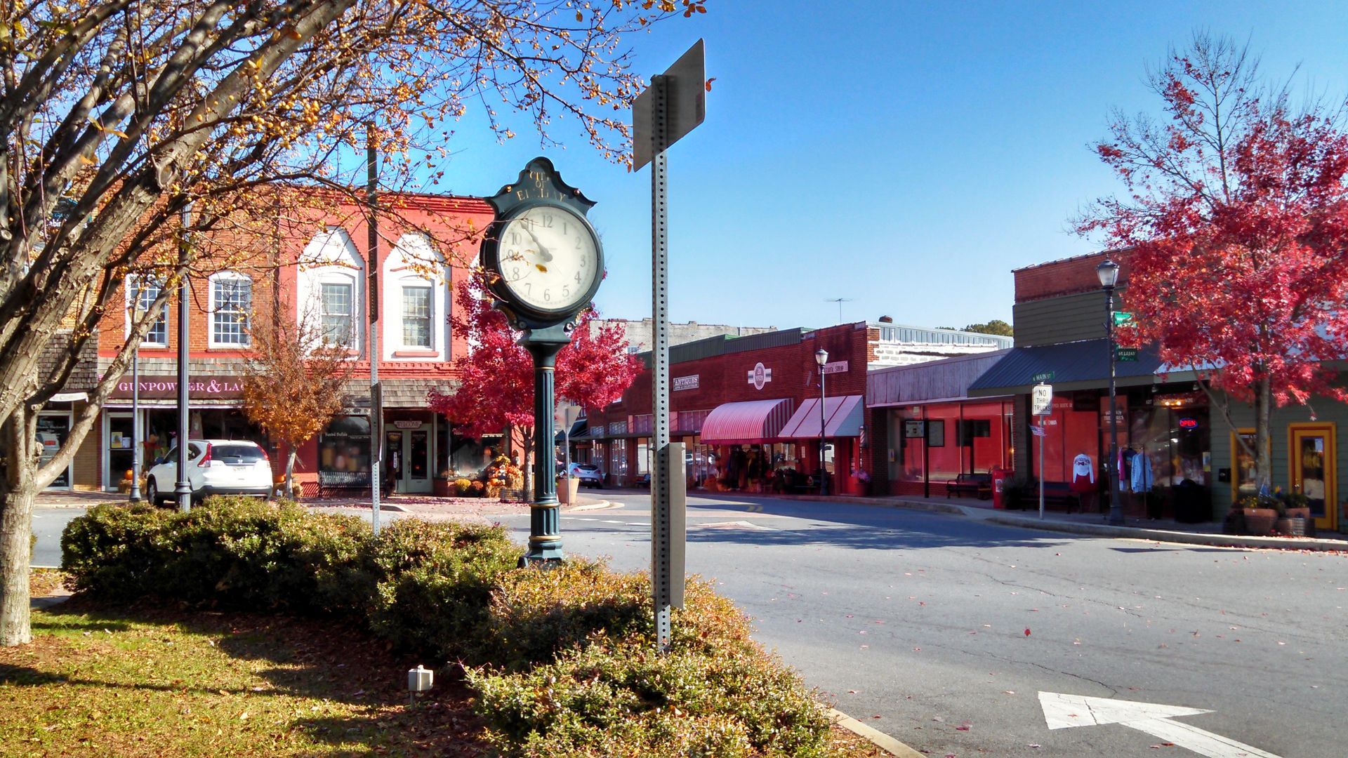 Ellijay Street scene with shops, clock, trees with red leaves, clear blue sky.