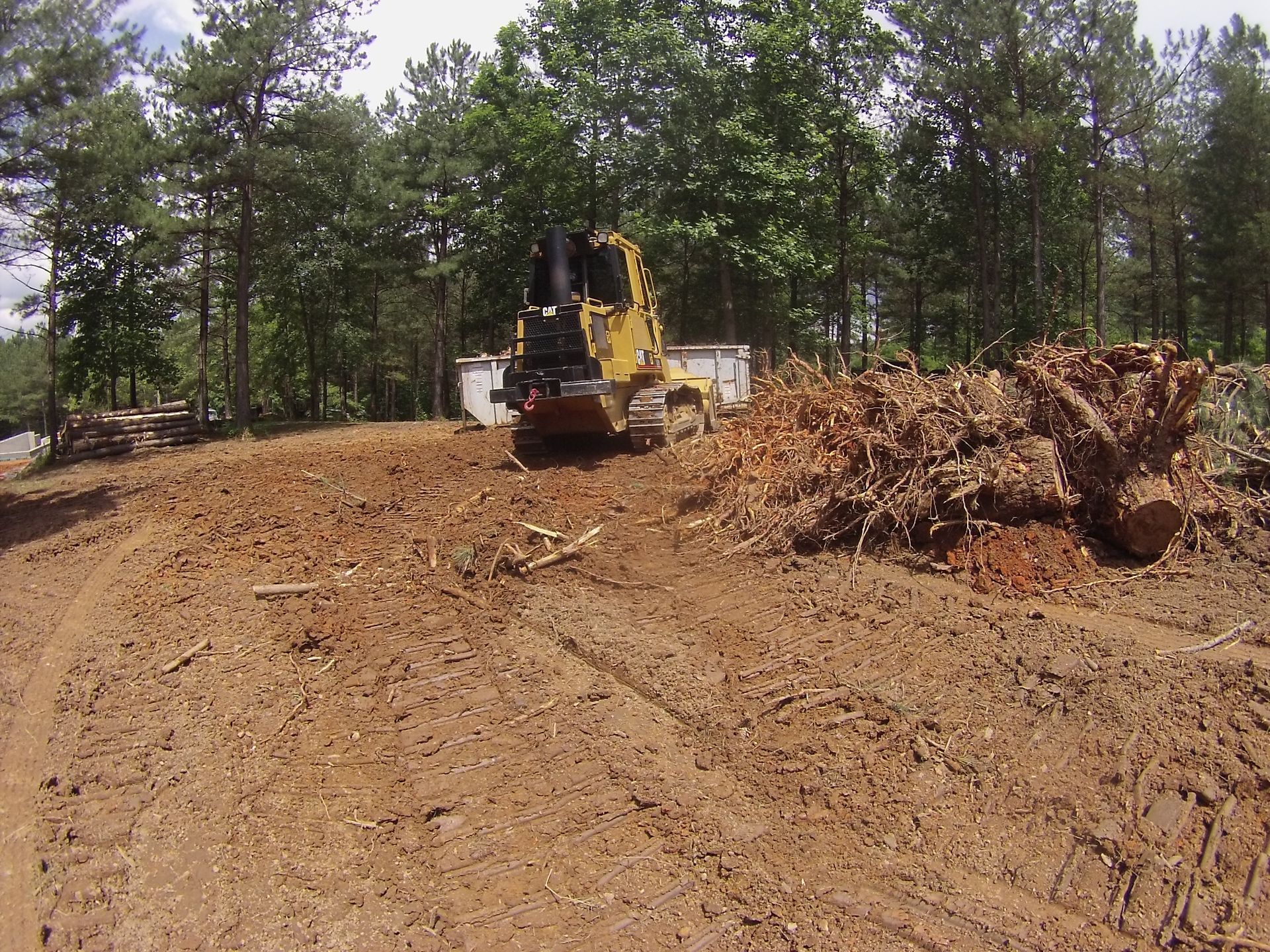 A bulldozer is driving through a dirt field with trees in the background