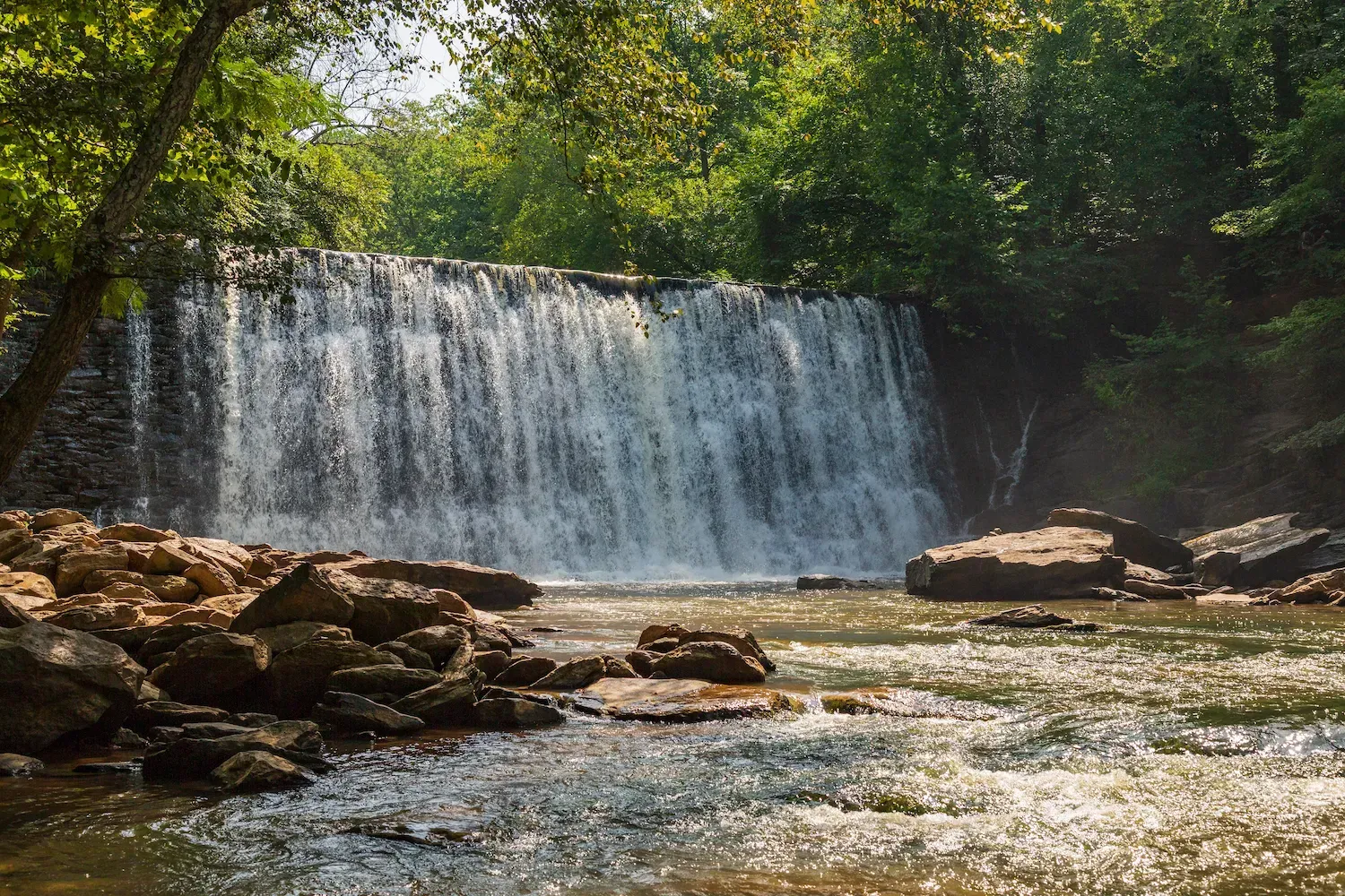 a waterfall in the middle of a river surrounded by trees in Roswell, Ga.