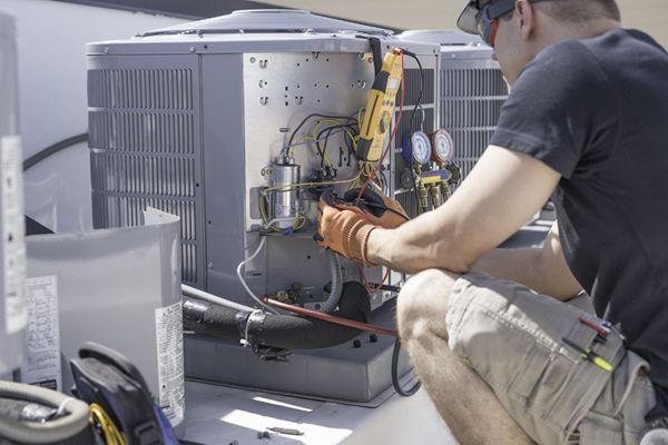 A man is working on an air conditioner on the roof of a building.