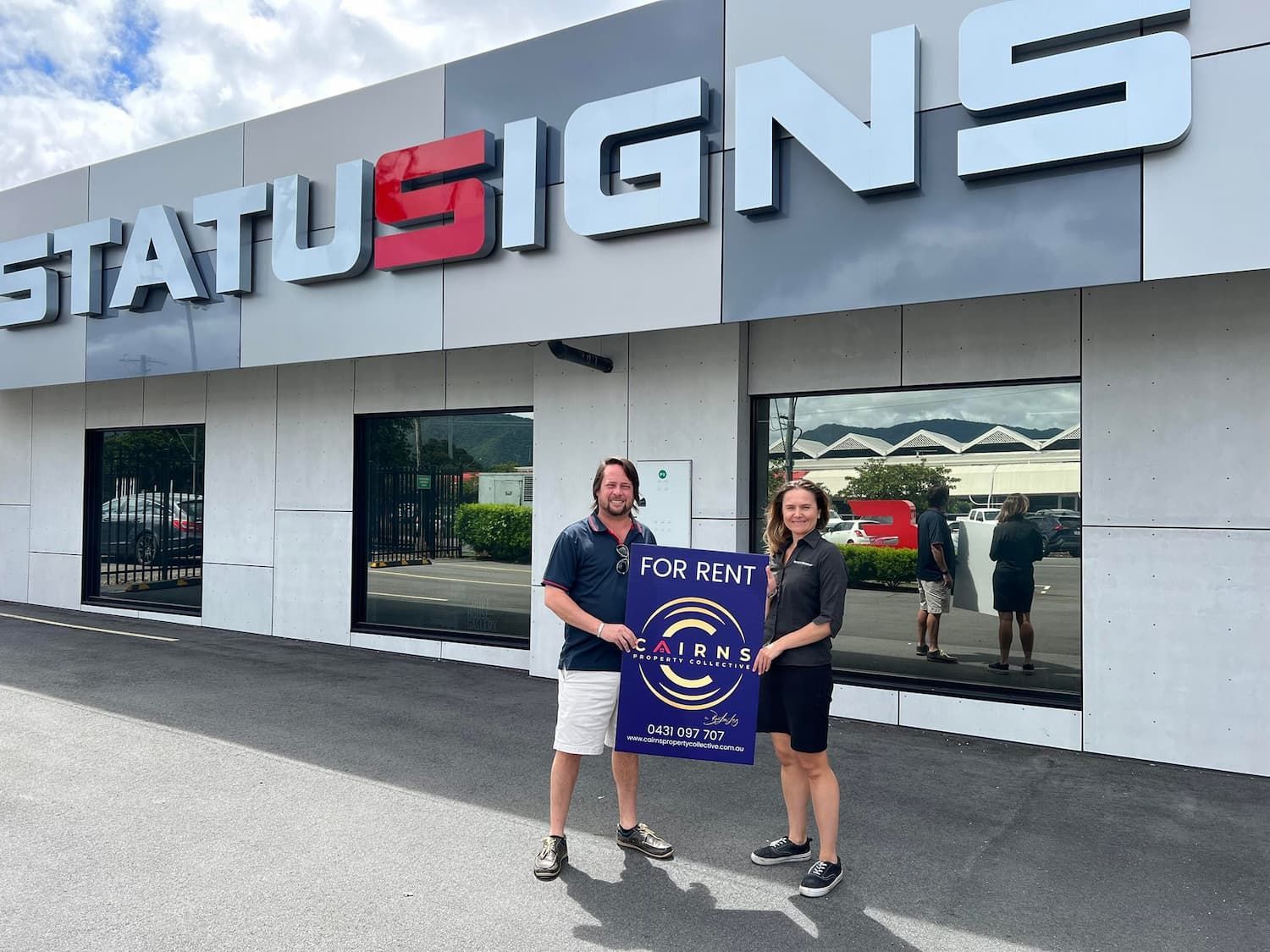A Man and Woman Are Standing in Front of A Building that Says Status Signs — Cairns Property Collective in Trinity Park, QLD