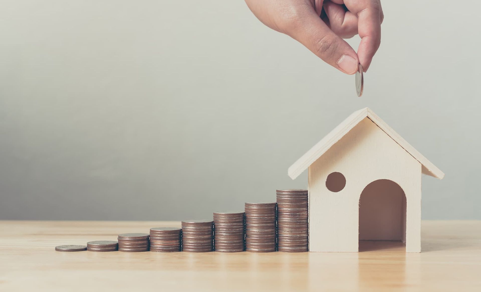 A Person Is Putting a Coin Into a Model House Next to Stacks of Coins — Cairns Property Collective in Trinity Park, QLD