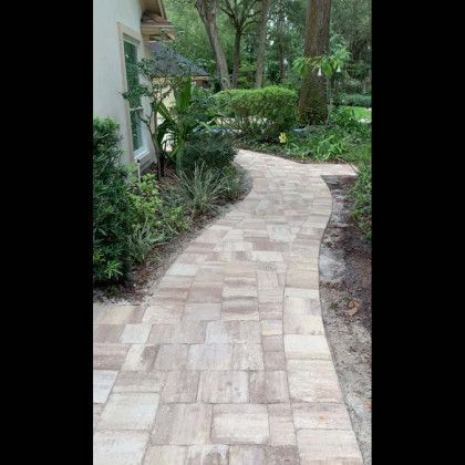 A brick walkway leading to a house surrounded by trees and bushes.