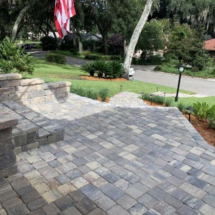 A brick walkway leading up to a house with a flag in the background.