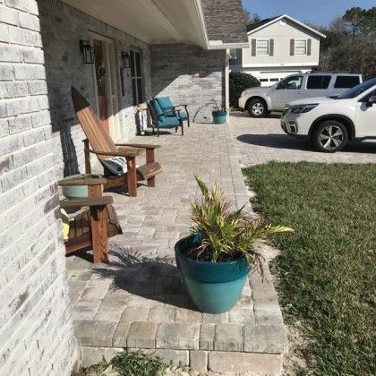 A porch with chairs and a potted plant in front of a house.
