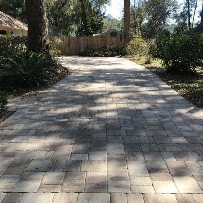 A brick driveway leading to a house surrounded by trees and bushes.