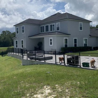 A large white house with a fence around it and two dogs in the backyard.