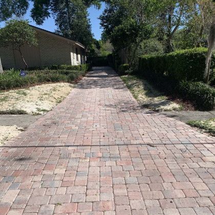 A brick driveway leading to a house with trees on both sides.