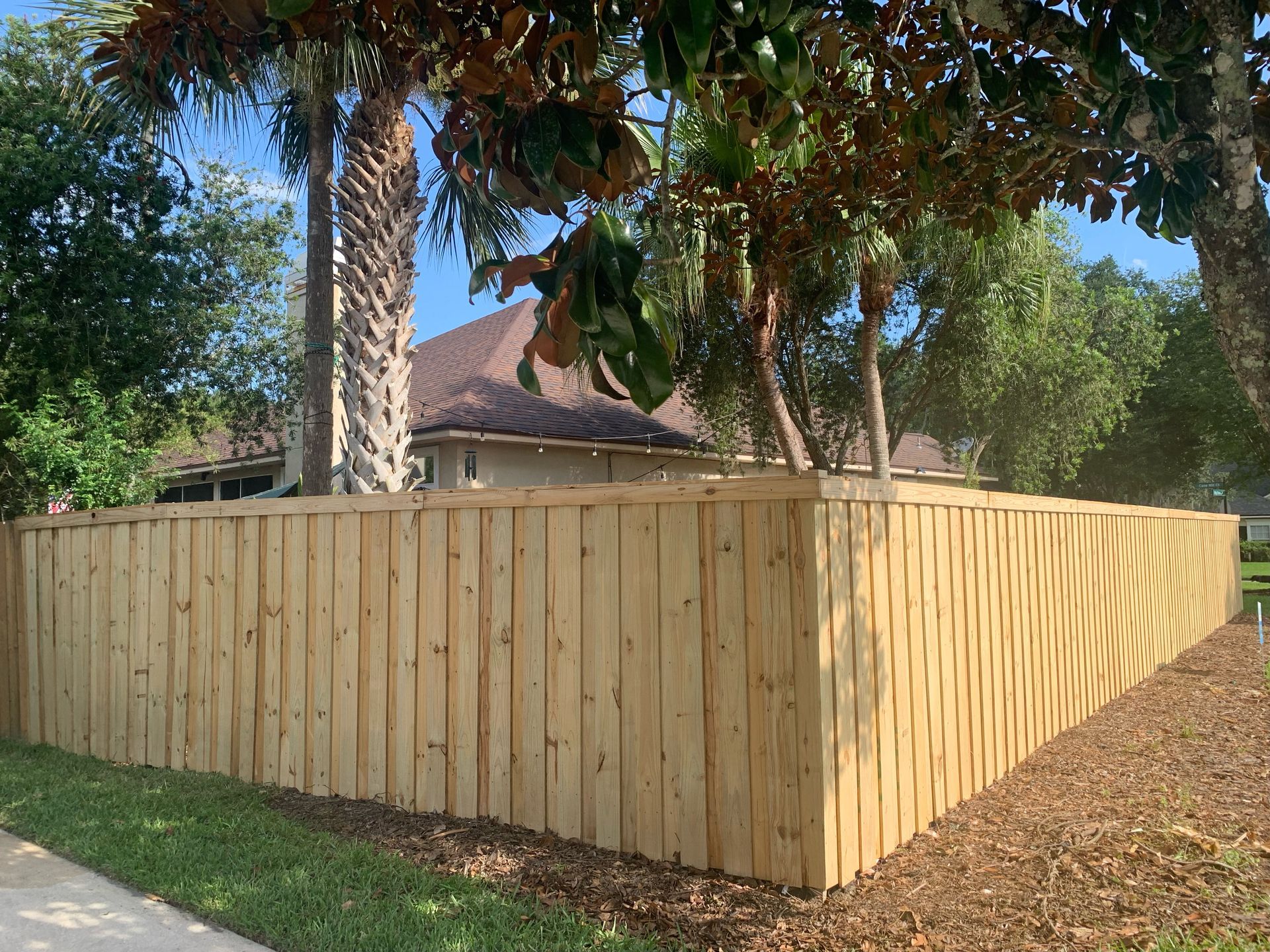 A wooden fence is surrounded by trees in front of a house.