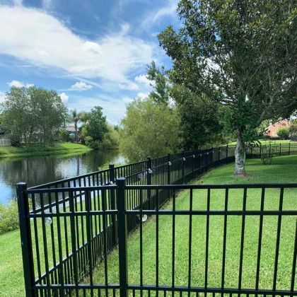 A black fence surrounds a lush green field next to a body of water.