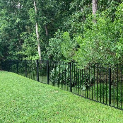 A black metal fence surrounds a lush green field.