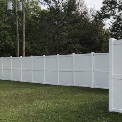 A white vinyl fence is sitting in the middle of a lush green field.