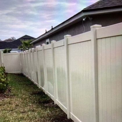 A white vinyl fence is in the backyard of a house.