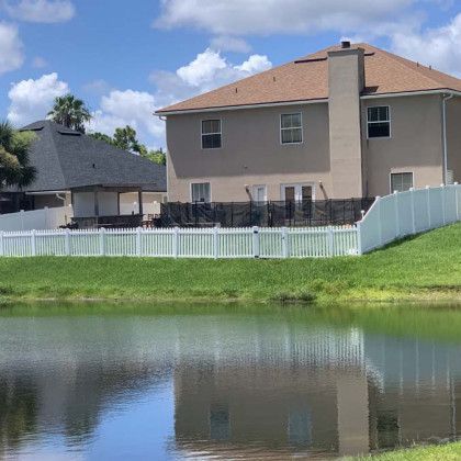 A house with a white picket fence and a pond in front of it.
